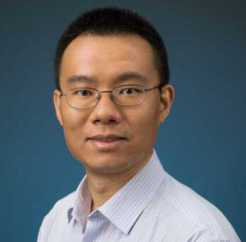 Dr. Xinhua Zhang smiles at camera in glasses and blue button up 