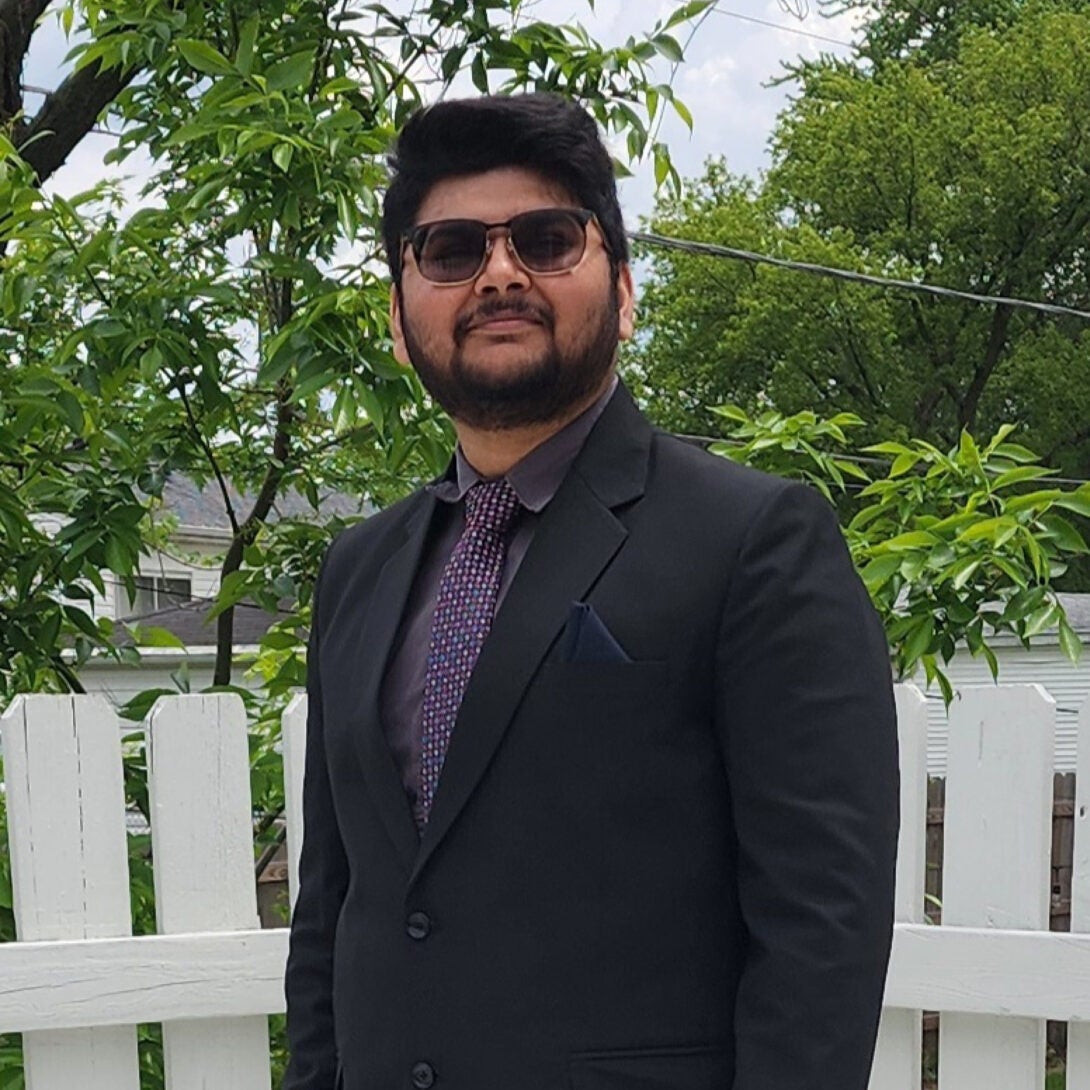 UIC MEng alum Shyamal Patel smiles in suit in front of white fence