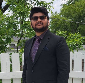 UIC MEng alum Shyamal Patel smiles in suit in front of white fence 